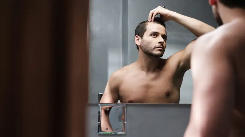saç ekimi sonrası güneşe çıkmak için aynaya bakan erkek