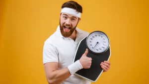 Obezite Ameliyatlarının Avantajları ve Dezavantajları- elinde tartı tutan mutlu bir adam